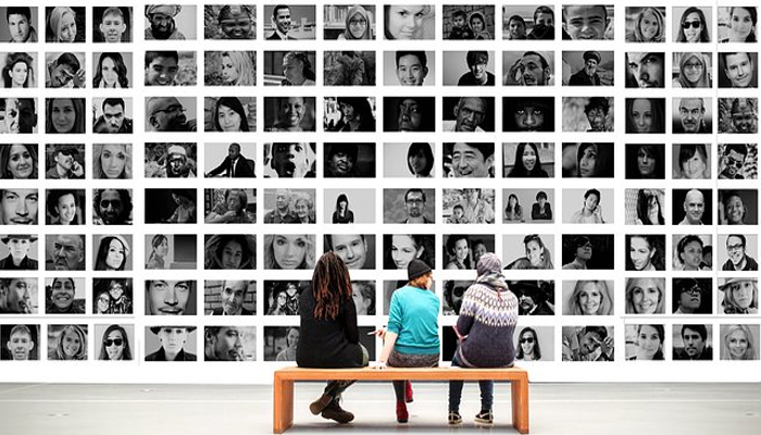3 people sitting on a bench in front of a wall with images of people.